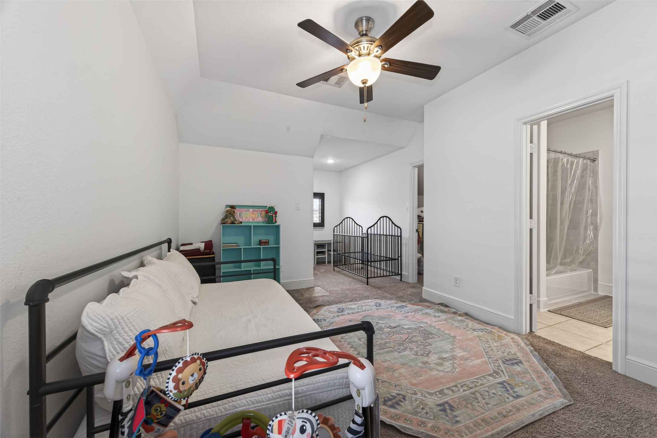 7014 Prairie Grass Lane Katy, TX 77493 - Photo 33 of 49 This spacious bedroom features neutral walls, a cozy carpet, and a ceiling fan. It includes a daybed, shelving, and a playpen, with an adjoining bathroom visible. The room is well-lit and has a comfortable, inviting atmosphere.