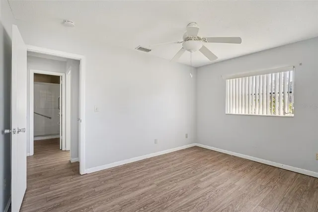 a view of an empty room with wooden floor and a ceiling fan