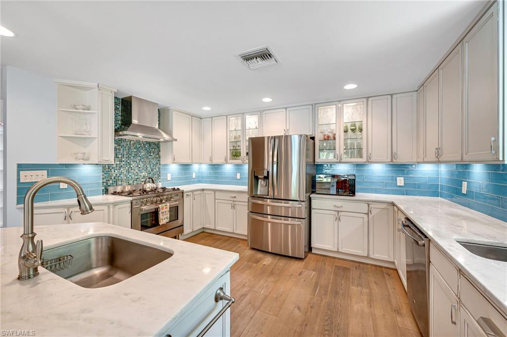 1155 12th Street North Naples, FL 34102 - Photo 8 of 18 Kitchen with stainless steel appliances, light stone counters, recessed lighting, glass insert cabinets, and light wood finished floors