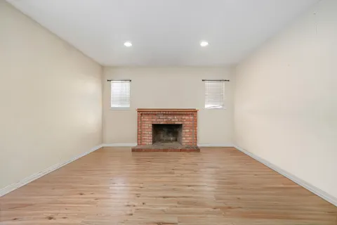 a view of an empty room with wooden floor fireplace and a window