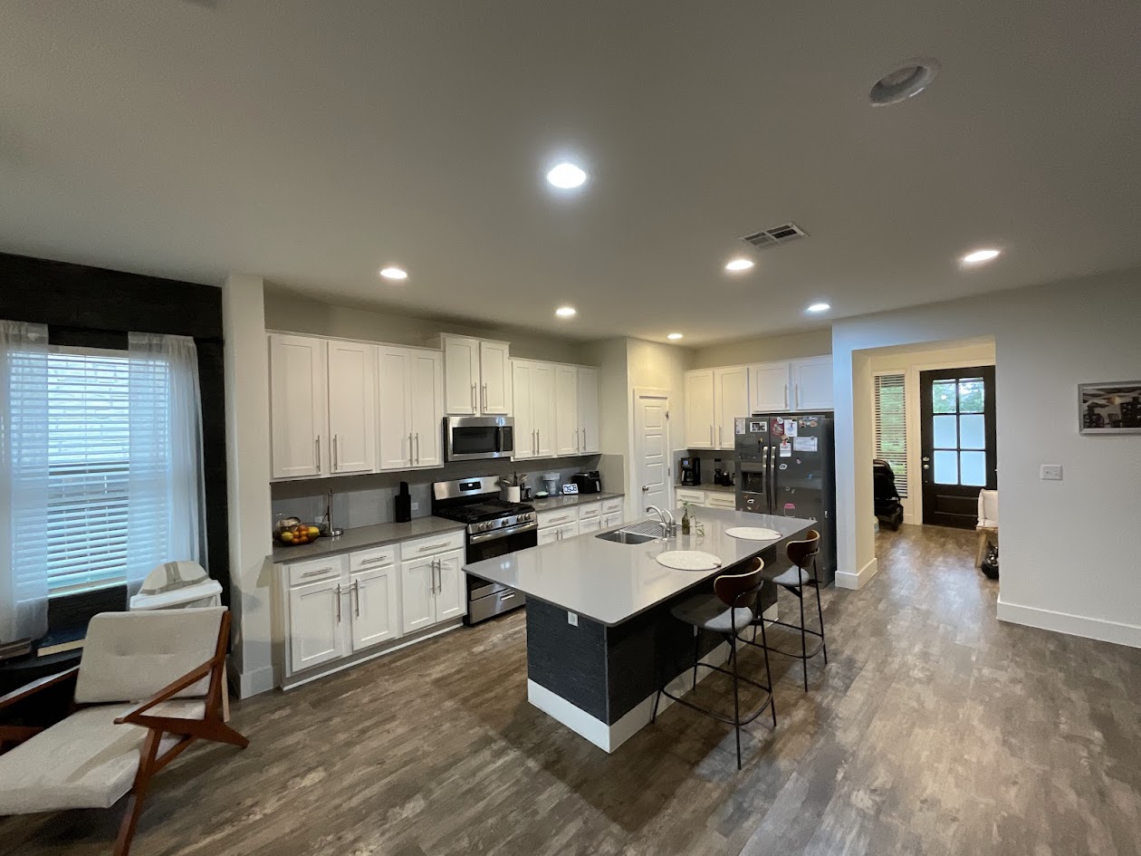 624 Golden Glory Road Leander, TX 78641 - Photo 18 of 39 Open-concept kitchen featuring an island with seating, stainless steel appliances, abundant white cabinetry, light-toned countertops, and wood-finish flooring