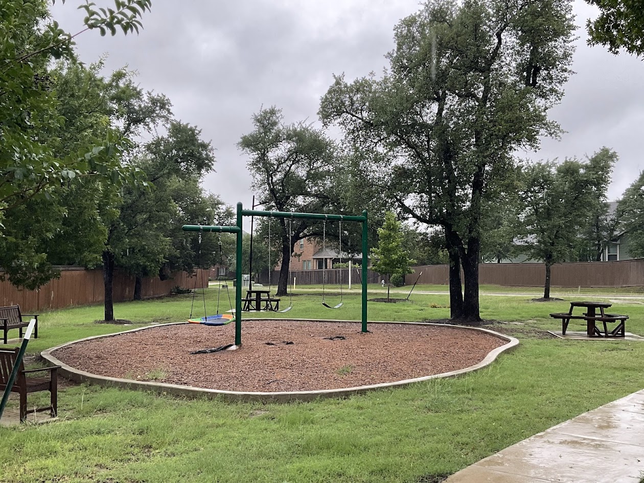 624 Golden Glory Road Leander, TX 78641 - Photo 34 of 39 Community green space featuring a swing set with a wood chip base, mature trees, and a concrete pathway