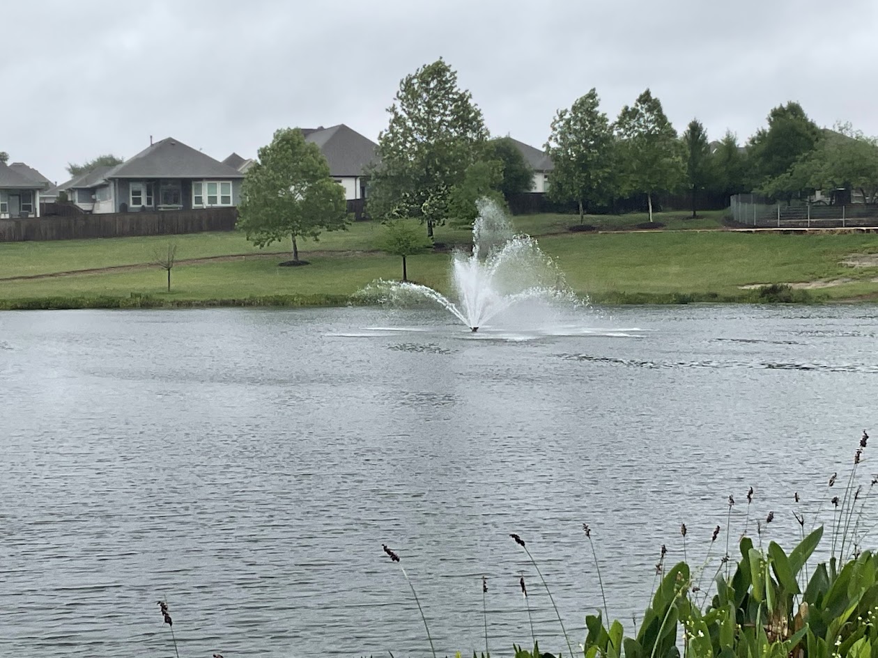 624 Golden Glory Road Leander, TX 78641 - Photo 35 of 39 Lakefront setting featuring a central fountain, surrounding green space, mature trees, residential structures, and established landscaping