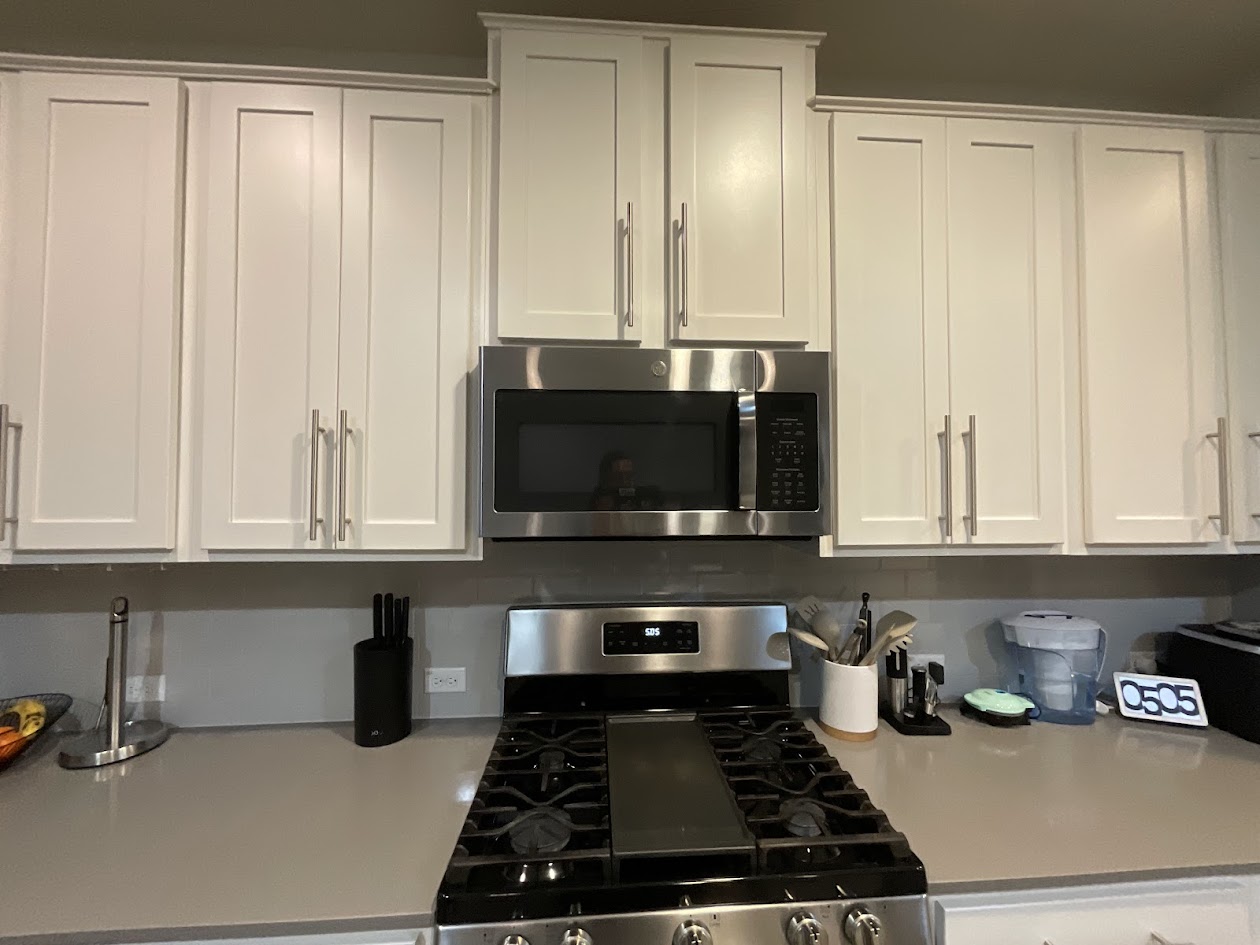 624 Golden Glory Road Leander, TX 78641 - Photo 5 of 39 Kitchen featuring white shaker-style cabinetry with crown molding, stainless steel microwave, gas range, and light-toned countertops