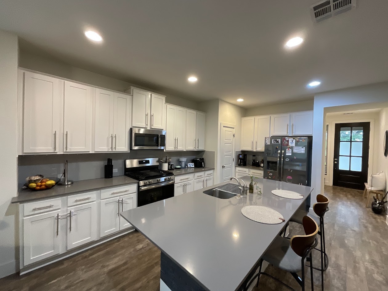 624 Golden Glory Road Leander, TX 78641 - Photo 9 of 39 Modern kitchen featuring an expansive island with a built-in sink, stainless steel appliances, abundant white cabinetry, light-toned countertops, and wood-finish flooring