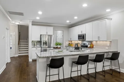 a kitchen with stainless steel appliances kitchen island granite countertop a stove a sink a refrigerator and white cabinets with wooden floor