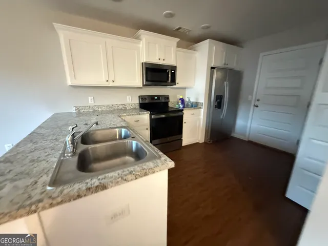 a kitchen with granite countertop a sink a stove top oven a refrigerator a counter space and cabinets