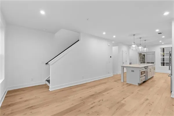 a view of an empty room and kitchen with wooden floor