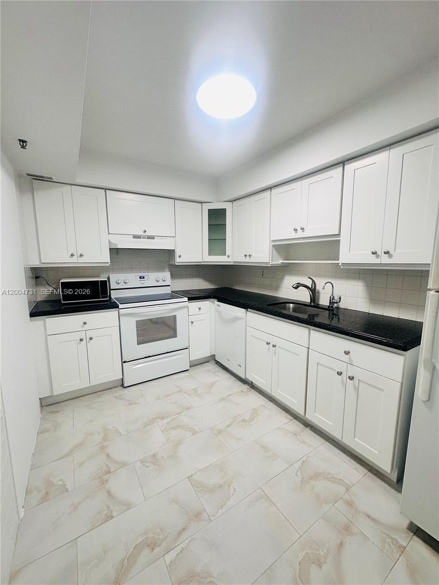 9511 Collins Avenue, Unit 1001 Surfside, FL 33154 - Photo 15 of 34 a kitchen with granite countertop a stove sink and cabinets