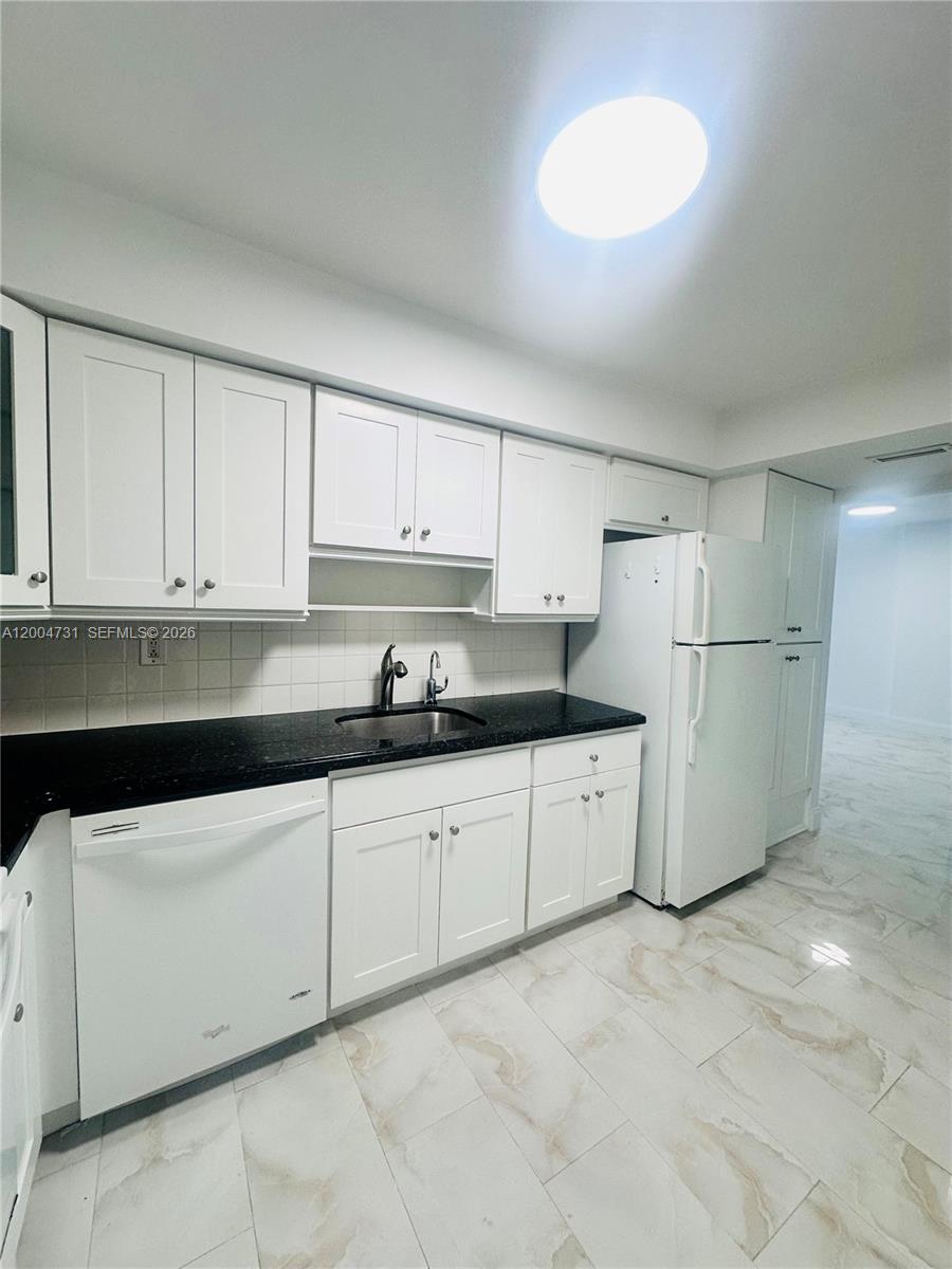 9511 Collins Avenue, Unit 1001 Surfside, FL 33154 - Photo 16 of 34 a kitchen with granite countertop a white refrigerator oven a sink and white cabinets