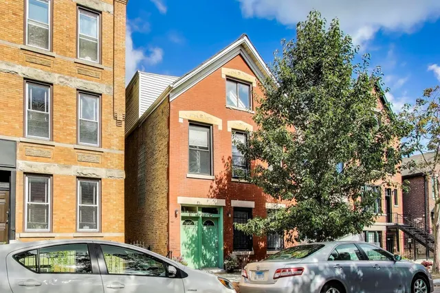 a front view of a building with trees and cars parked