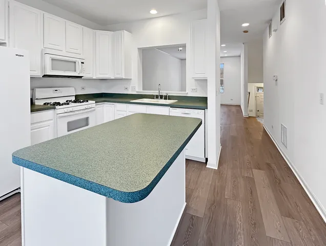 a kitchen with stainless steel appliances granite countertop a refrigerator a sink dishwasher a stove and white countertops with wooden floor