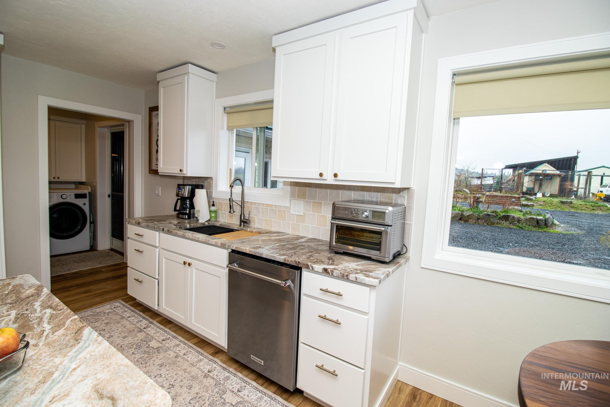 5404 Freeman Creek Road Lenore, ID 83541 - Photo 20 of 50 Kitchen featuring white cabinetry, light stone counters, washer / dryer, stainless steel dishwasher, and light wood-style floors
