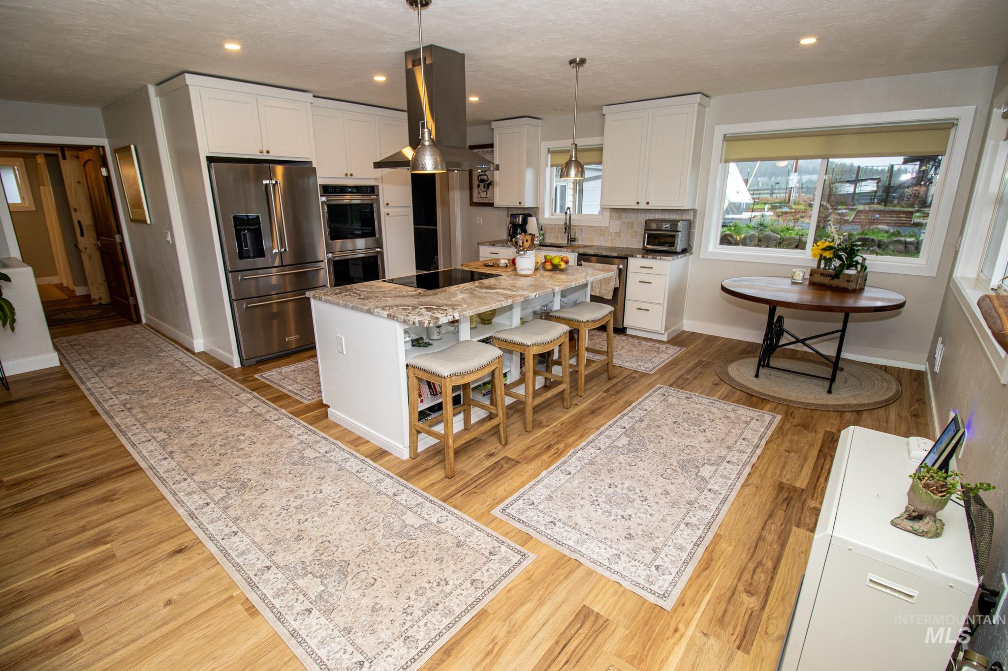 5404 Freeman Creek Road Lenore, ID 83541 - Photo 21 of 50 Kitchen featuring stainless steel appliances, white cabinetry, island range hood, light stone countertops, and a kitchen island