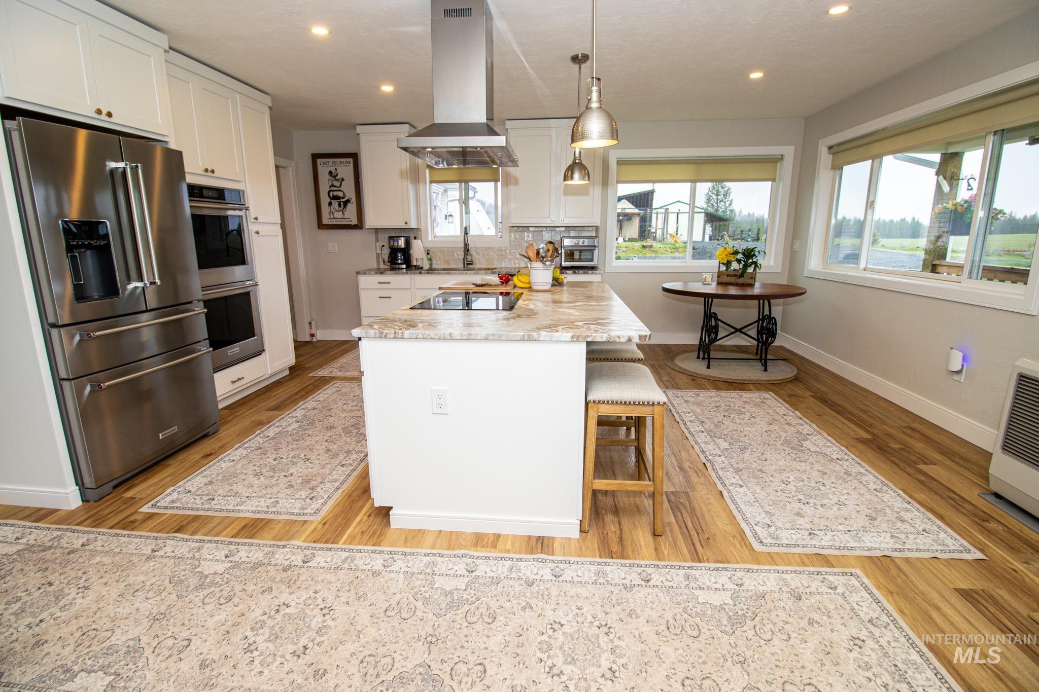 5404 Freeman Creek Road Lenore, ID 83541 - Photo 24 of 50 Kitchen with stainless steel appliances, light stone countertops, island exhaust hood, a kitchen bar, and white cabinetry