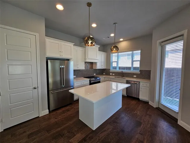 a large kitchen with granite countertop a refrigerator a stove a sink dishwasher and white cabinets with wooden floor