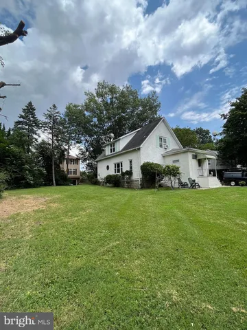a view of a white house in front of a big yard with plants and large trees