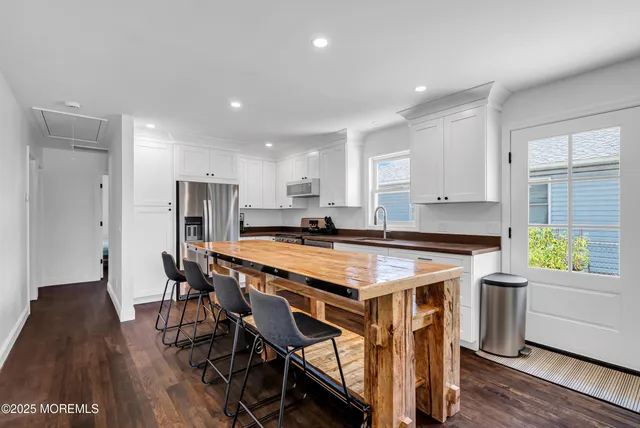 a kitchen with kitchen island a stove a refrigerator a sink a dining table and chairs with wooden floor