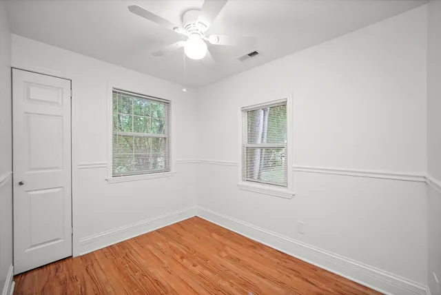 an empty room with wooden floor chandelier fan and windows
