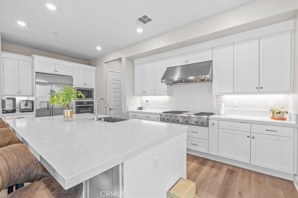 113 Source Irvine, CA 92618 - Photo 12 of 39 a kitchen with stainless steel appliances a stove a sink a refrigerator and white cabinets with wooden floor