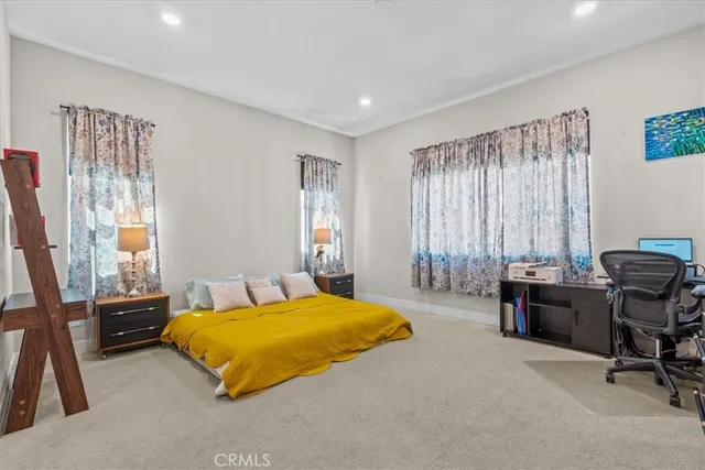 a bedroom with a bed a desk and chair with windows