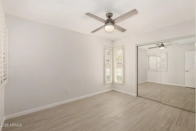 an empty room with wooden floor fan and windows