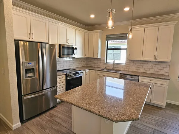a kitchen with granite countertop a refrigerator a sink a stove a microwave and island