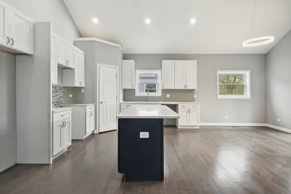 a kitchen with kitchen island granite countertop a refrigerator a sink a stove and white cabinets with wooden floor
