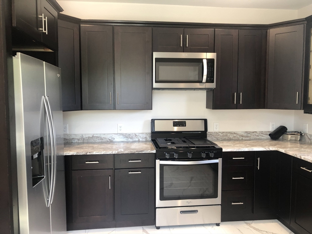 28-32 Calvary Street Waltham, MA 02453 - Photo 4 of 41 a kitchen with granite countertop stainless steel appliances and wooden cabinets