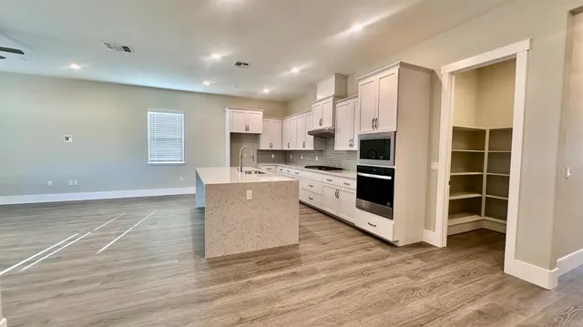 a large kitchen with kitchen island a sink wooden floor and stainless steel appliances