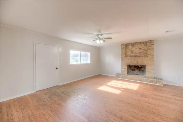 a view of an empty room with wooden floor fireplace and a window