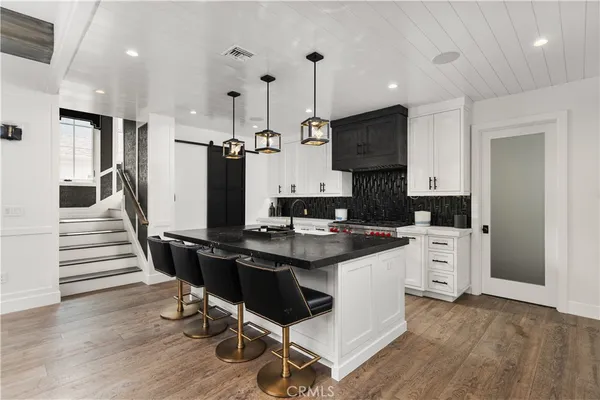 a kitchen with stainless steel appliances a stove top oven a refrigerator a sink and white cabinets with wooden floor