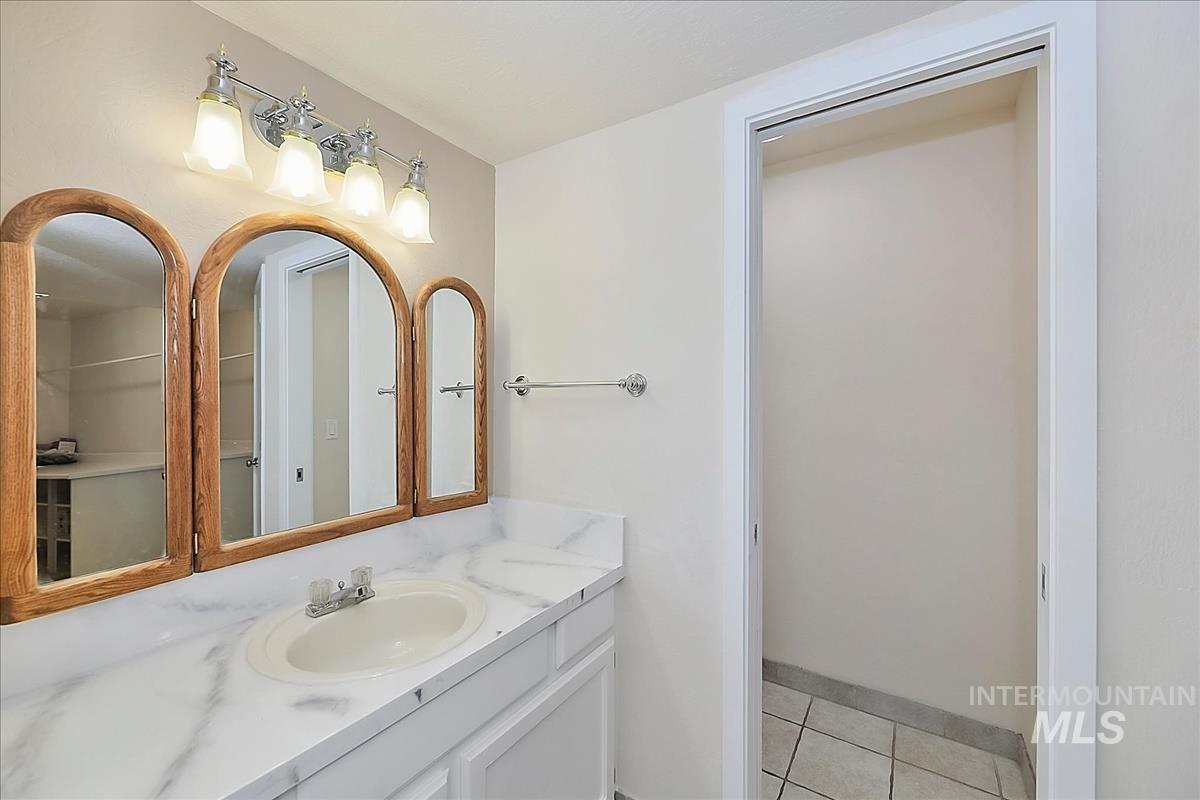 2804 West Sunrise Rim Road Boise, ID 83705 - Photo 25 of 50 Bathroom vanity featuring a white countertop with subtle veining, an integrated sink, and an arched three-panel mirror