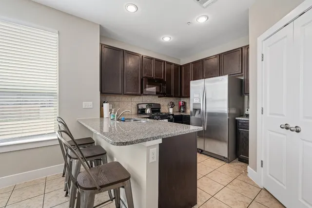 a kitchen with stainless steel appliances granite countertop a refrigerator a stove a sink a dining table and chairs