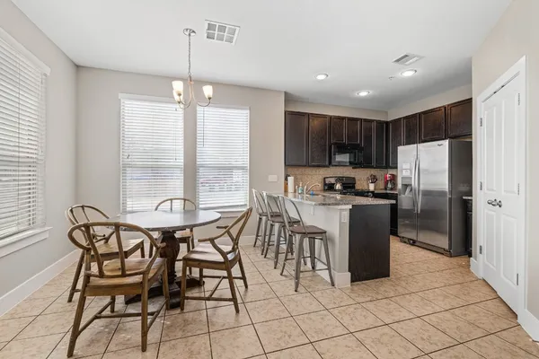 a kitchen with granite countertop a refrigerator a stove a sink a dining table and chairs