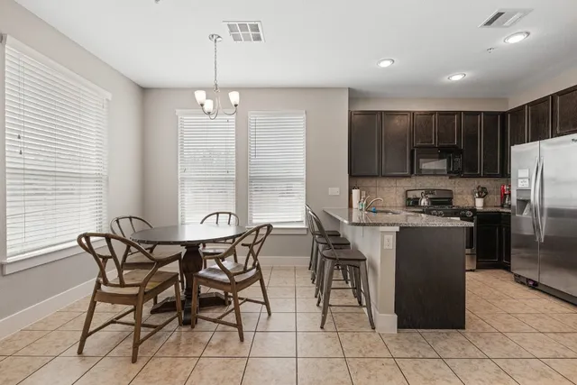 a kitchen with stainless steel appliances granite countertop a refrigerator a stove a sink a dining table and chairs