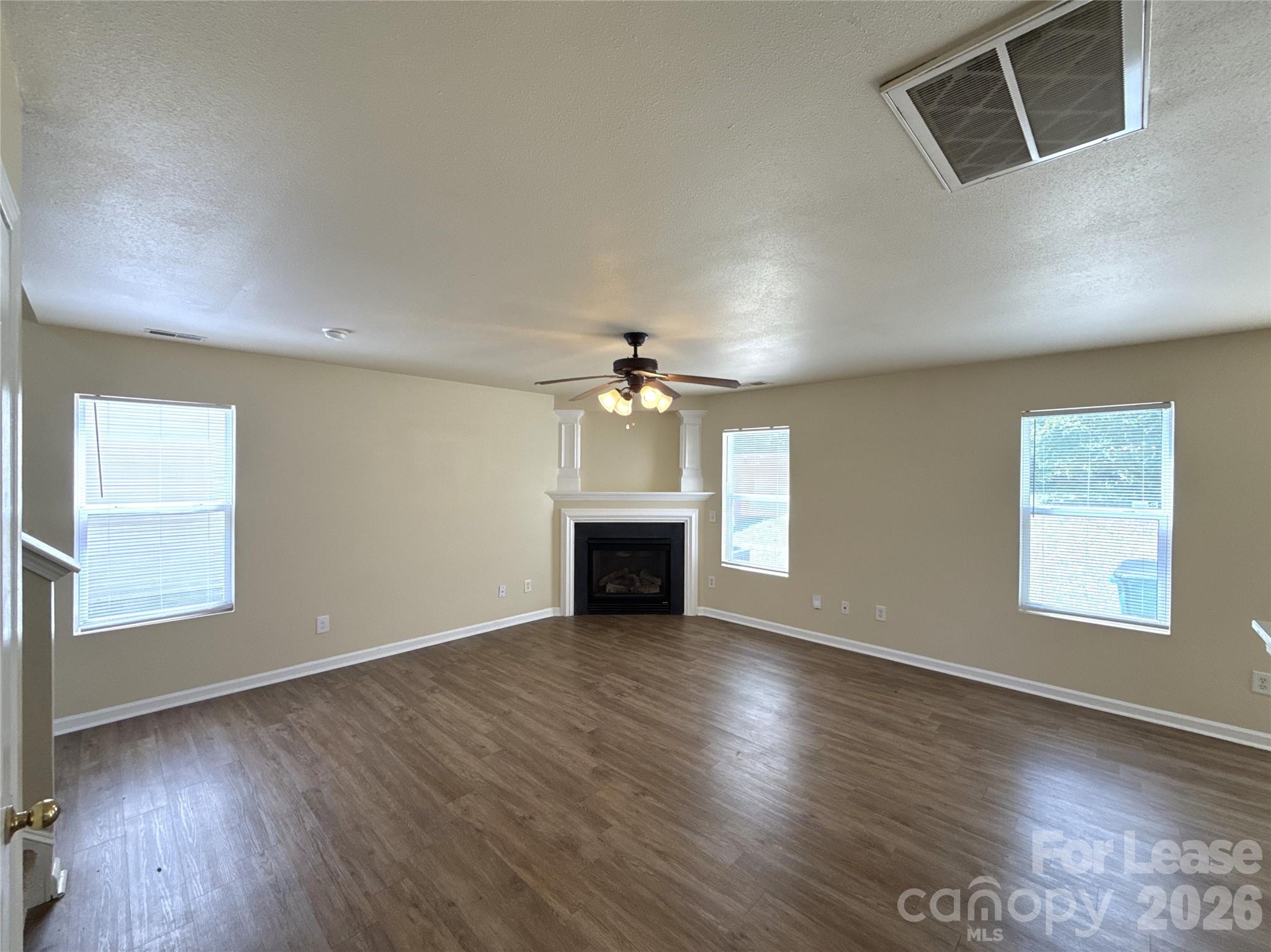 6831 Sunman Road Charlotte, NC 28216 - Photo 2 of 14 an empty room with wooden floor fireplace and windows