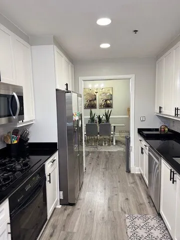 a kitchen with stainless steel appliances granite countertop a stove top oven a sink dishwasher a dining table and chairs with wooden floor