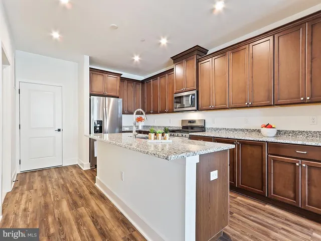 a kitchen with stainless steel appliances granite countertop a refrigerator a sink dishwasher a stove and white countertops with wooden floor