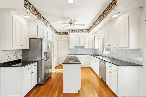 a kitchen with granite countertop a refrigerator a sink dishwasher a stove and white cabinets with wooden floor