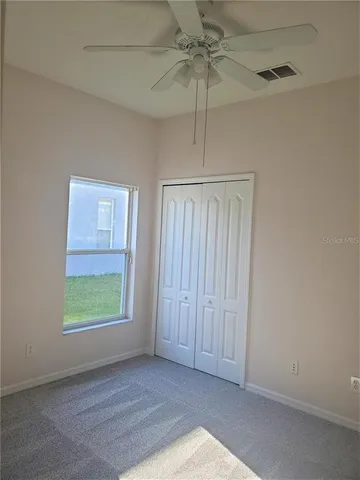 an empty room with chandelier fan and windows