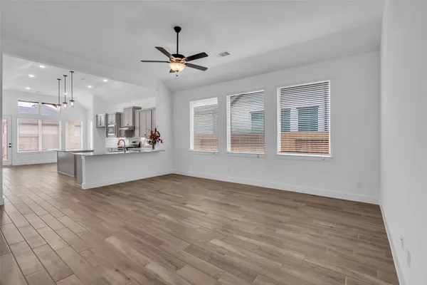 a view of an empty room with wooden floor and a kitchen