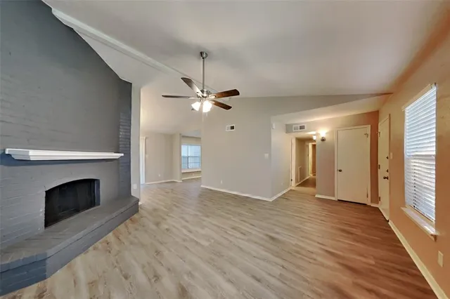 an empty room with wooden floor fireplace and windows