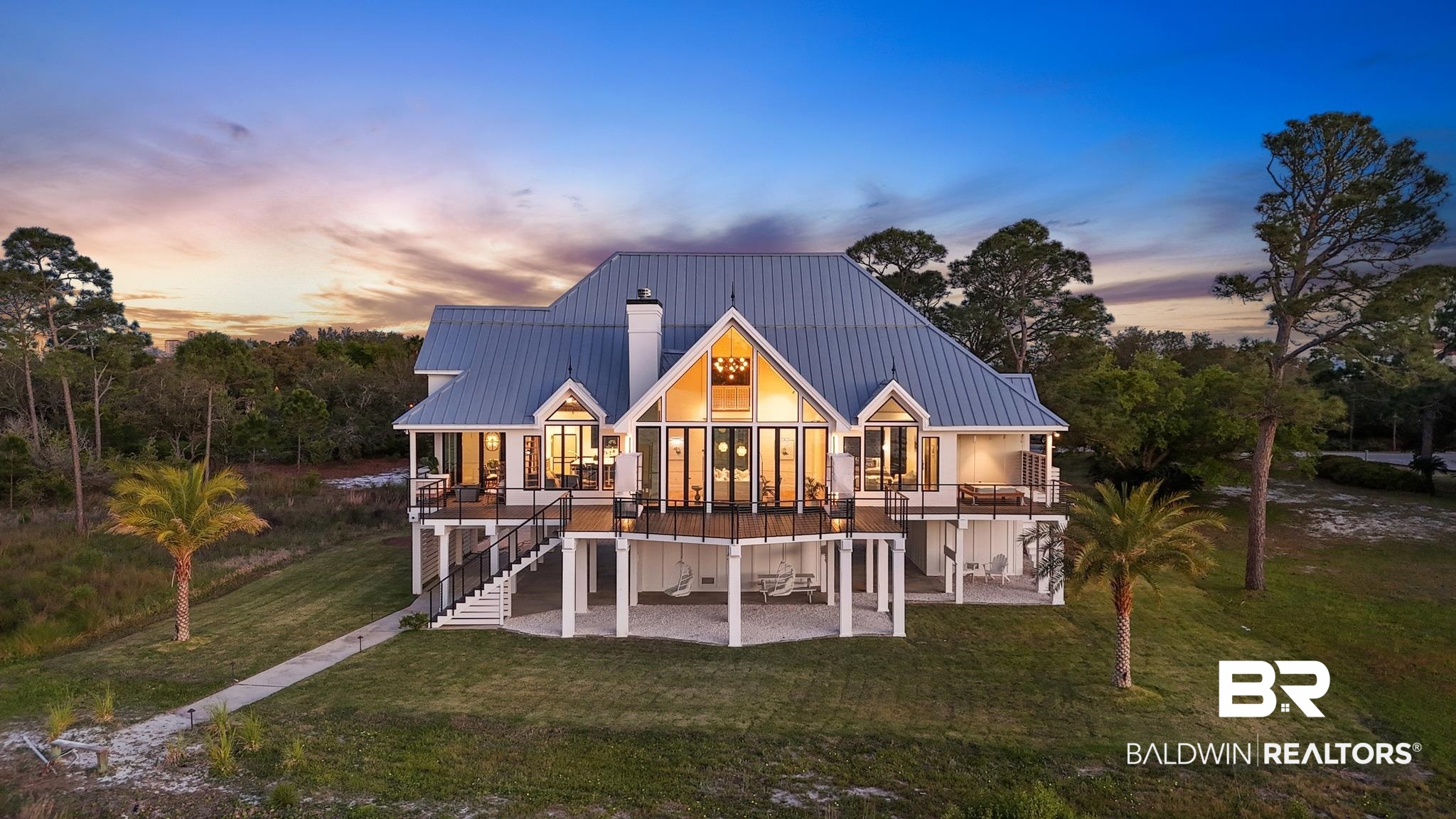 33349 River Road Orange Beach, AL 36561 - Photo 54 of 61 Striking elevated residence featuring a metal roof, expansive windows, multiple outdoor balconies, covered patio areas, and a prominent chimney