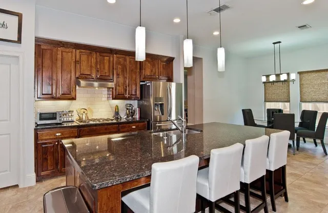 a kitchen with stainless steel appliances granite countertop a stove top oven a refrigerator a sink a dining table and chairs with wooden floor