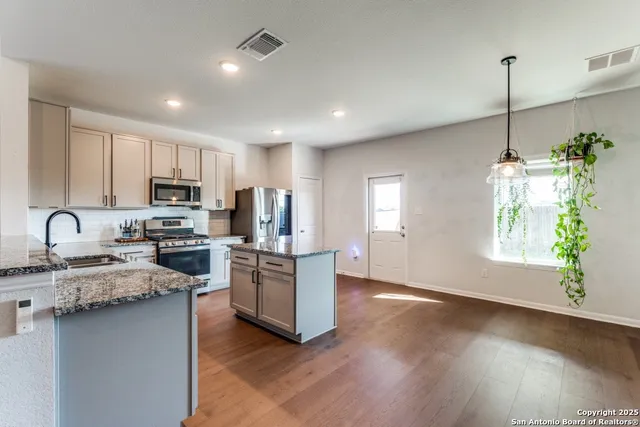 a kitchen with stainless steel appliances granite countertop a refrigerator a sink dishwasher a stove and white cabinets with wooden floor