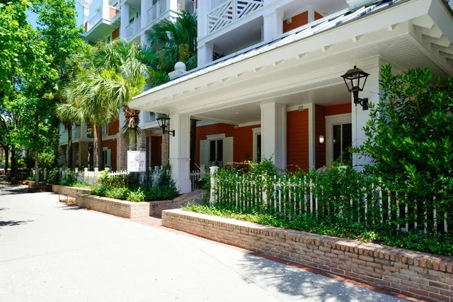 a view of a white house with a large windows plants and large trees