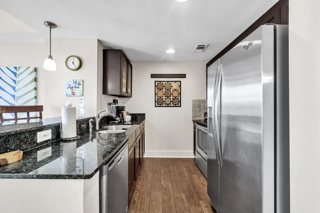 a kitchen with stainless steel appliances granite countertop a refrigerator a stove and a sink with wooden floor