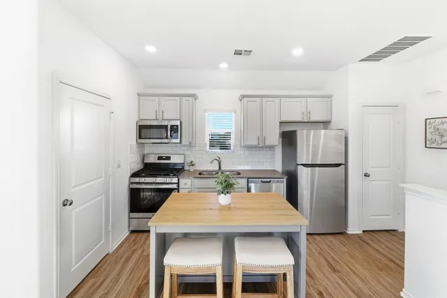 a kitchen with stainless steel appliances granite countertop a dining table chairs refrigerator and sink