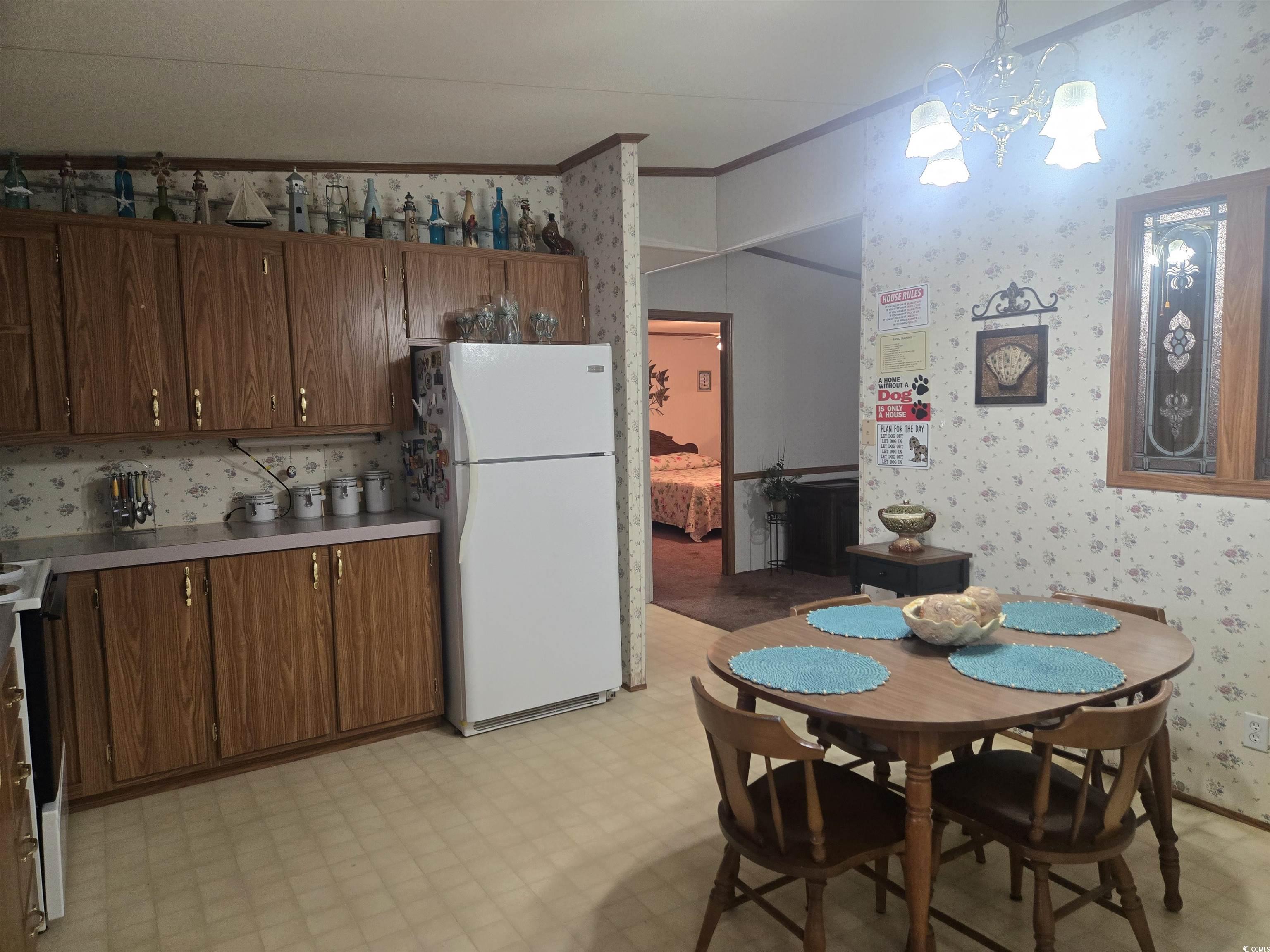 326 Tunnoch Road Murrells Inlet, SC 29576 - Photo 10 of 22 Kitchen with wallpapered walls, light flooring, freestanding refrigerator, crown molding, and a chandelier